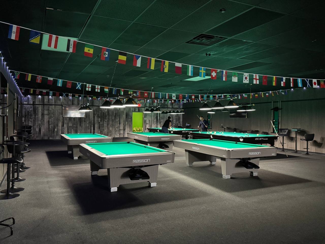 The billiards room at VIP BILLIARDS with green tables and hanging lights